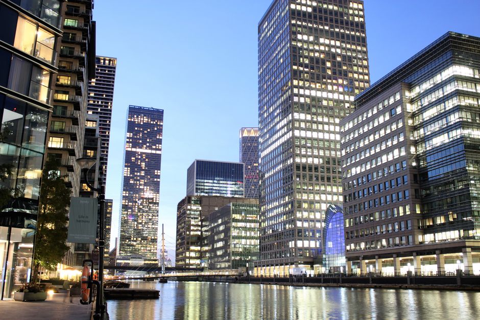 Photograph of modern high-rise residential buildings along the waterfront with varied architectural designs, including some with curved and angular facades, under a partly cloudy sky during daylight. 
