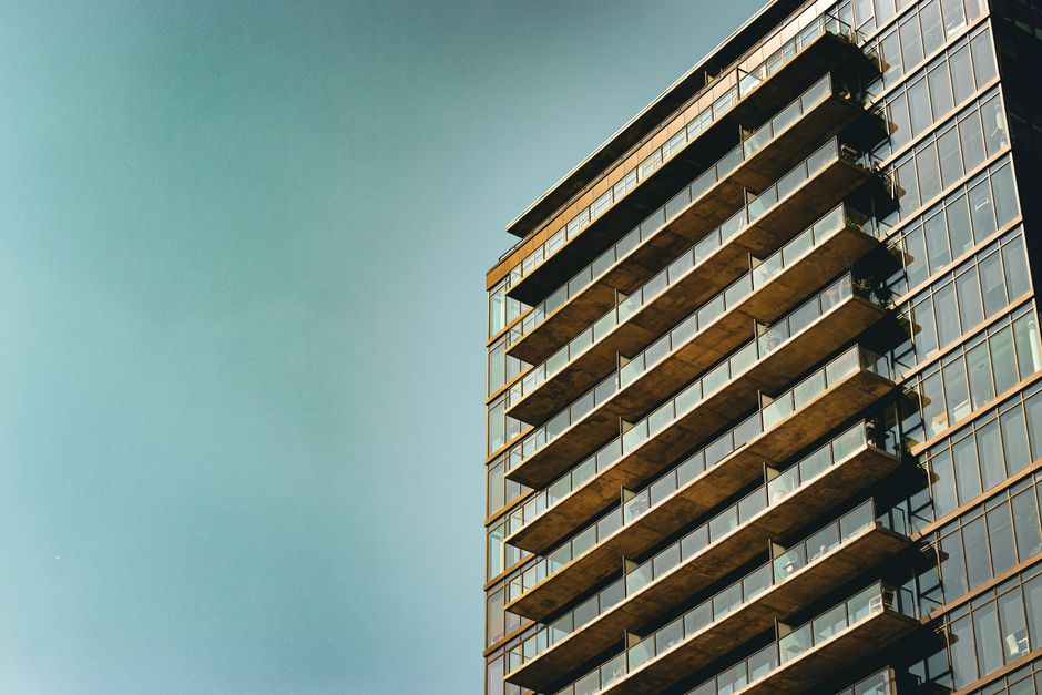 Exterior view of a high-rise residential building with a modern design, featuring numerous glass windows and balconies. The structure has a combination of white and glass facades, reflecting the blue 